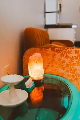 The waiting room at Good Body Massage, with an orange couch, a green glass topped side table with a salt lamp and business card holder on top.