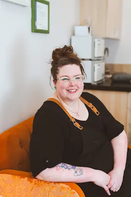 Kelli sitting on an orange couch, smiling.